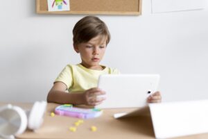 Niño sentado en una mesa, completamente absorto mirando la pantalla de una tablet.
